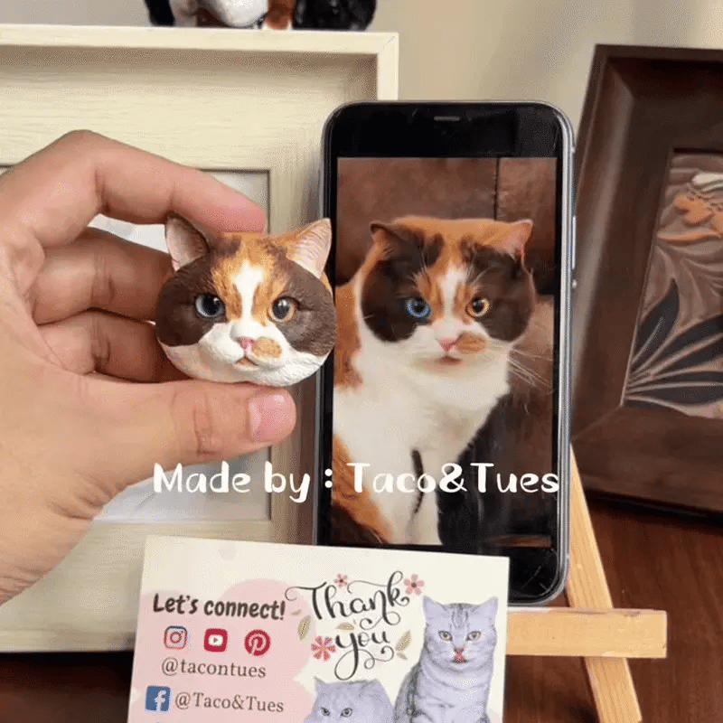 Hand holding a custom hand-painted cat figurine next to real cat photo on phone, showing accurate likeness, made by Taco&Tues