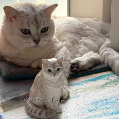 Elegant silver shaded cat sculpture by TaconTues, sitting beside real cat on cushion — bespoke pet memorial art capturing serene moments for cat parents